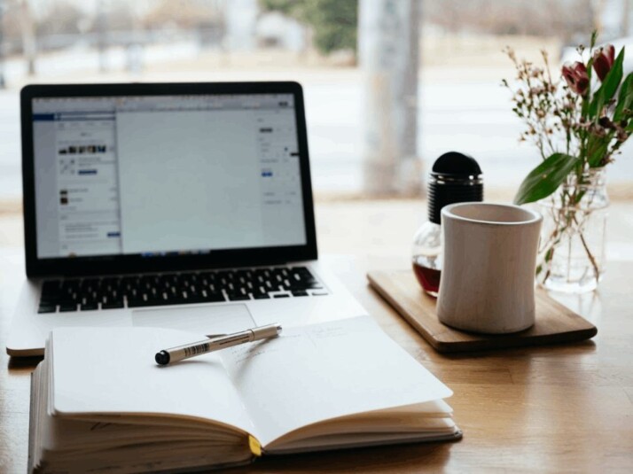 A MacBook Pro near a white open book on wooden table