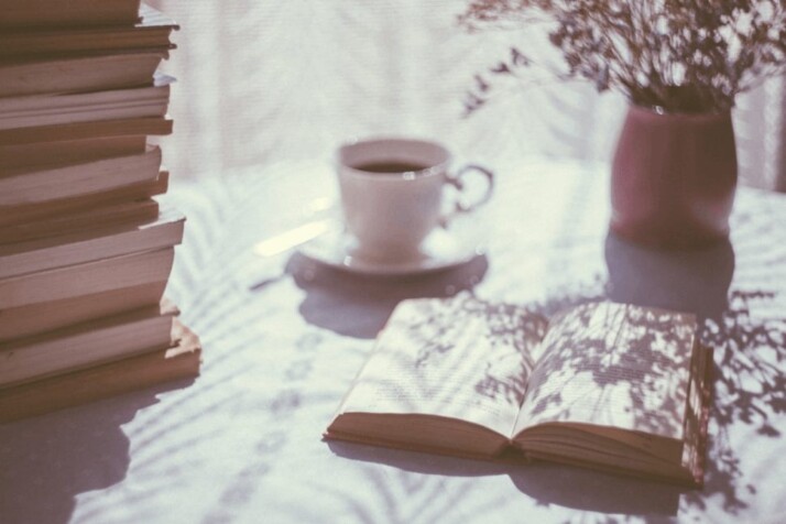 An open book beside white ceramic teacup on saucer