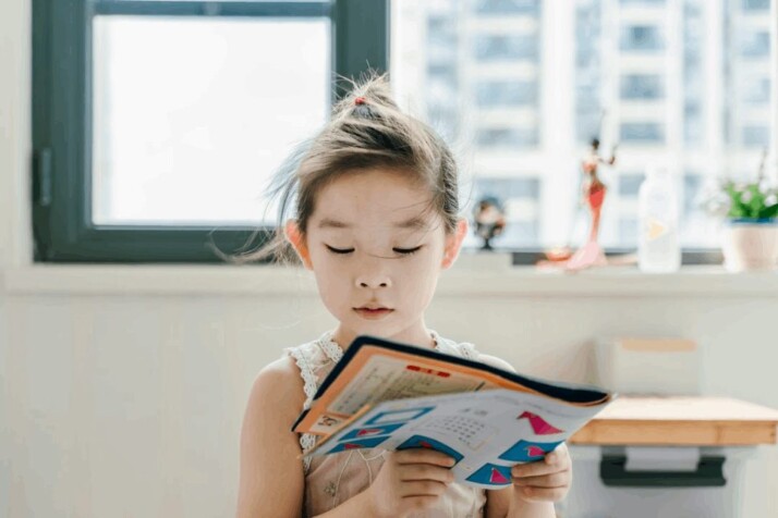 Kindergartner reading a book to develop reading skills at an early age.