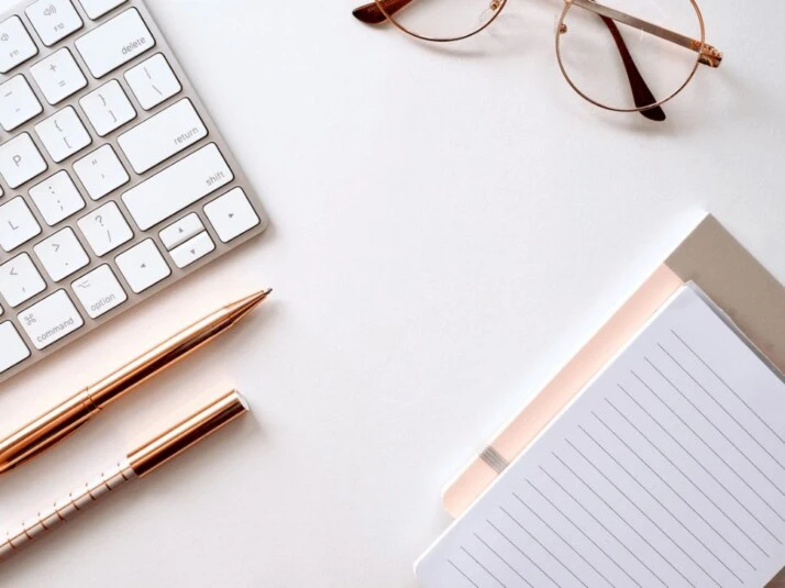 A pen near a keyboard, black lined paper, and eyeglasses