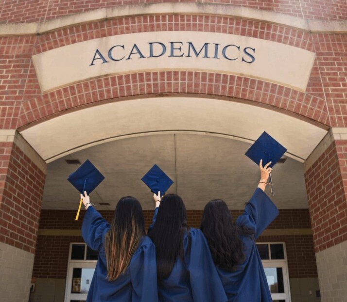 Students standing before school hall after successfully graduating. They look like they are celebrating.