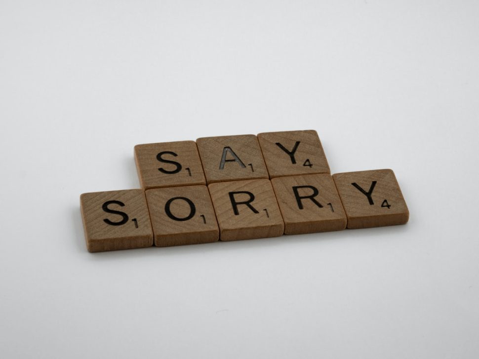 Say Sorry brown wooden scrabble blocks on a white surface.
