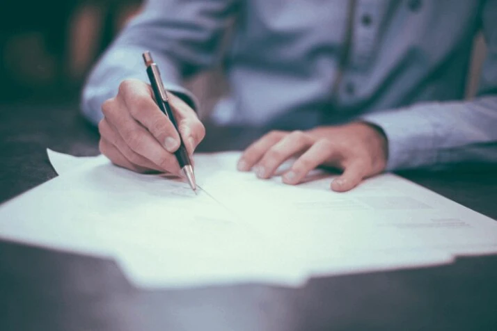 A man in a blue shirt writing on a paper