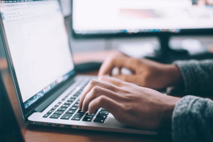 A person in gray garment typing on a MacBook Pro