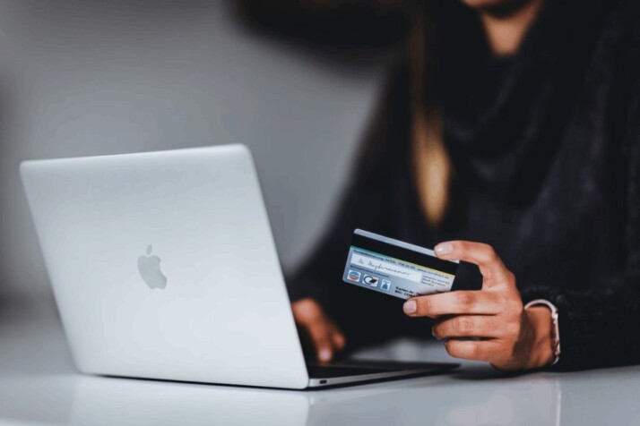 woman holding a credit card near silver macbook laptop