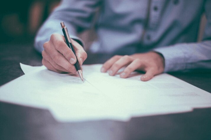 man with a blue cotton shirt writing on paper