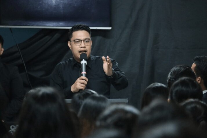 man in black long sleeve shirt holding microphone speaking to a crowd