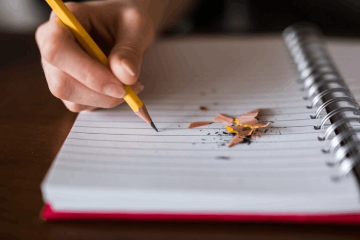 A person holding a pencil and writing on a notebook