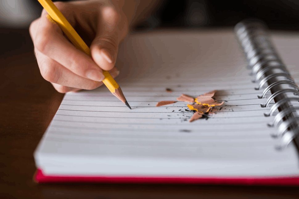 A person holding a pencil and writing on a notebook