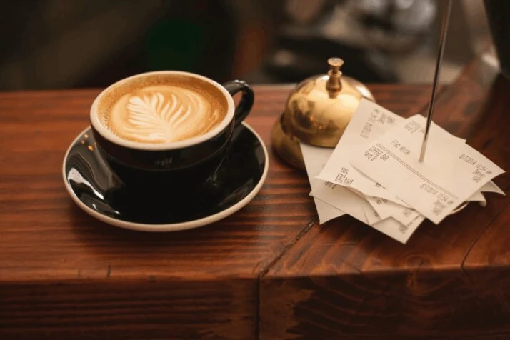 black ceramic cup with saucer and cappuccino on brown wooden surface