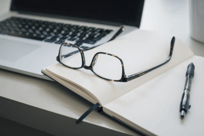 A black framed eyeglasses and black pen on a notebook