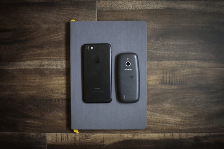 black iPhone 7 next to a Nokia 3310, on top of a book