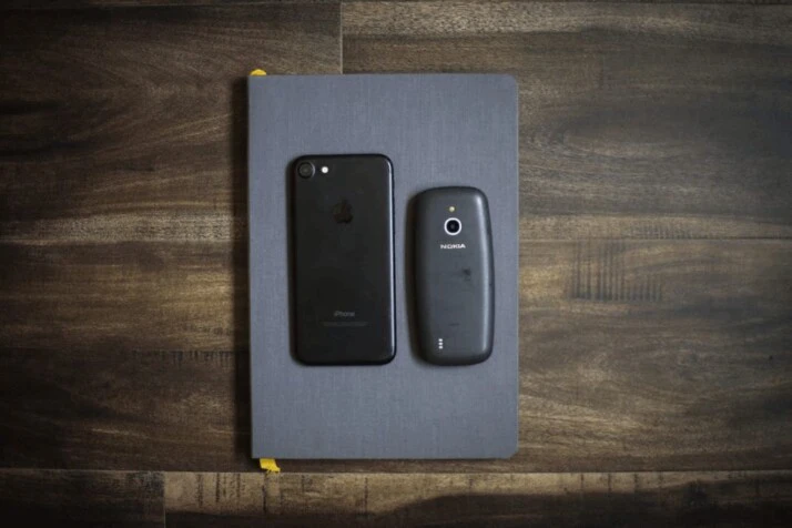 black iPhone 7 next to a Nokia 3310, on top of a book