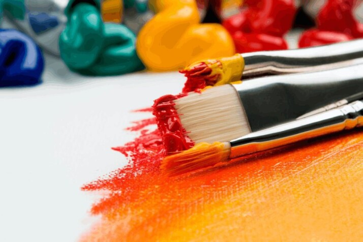 three silver paint brushes on white textile with other art materials