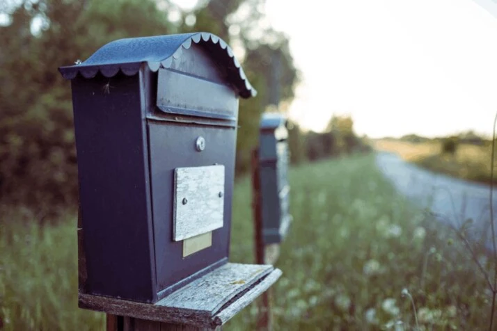 A black mail box on the side of a road.