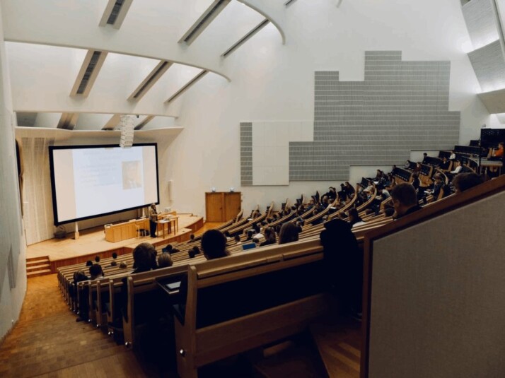 people sitting in lecture hall listening to a presentation by their teacher.