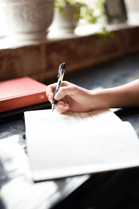 a woman using a ball point pen to write on a notebook