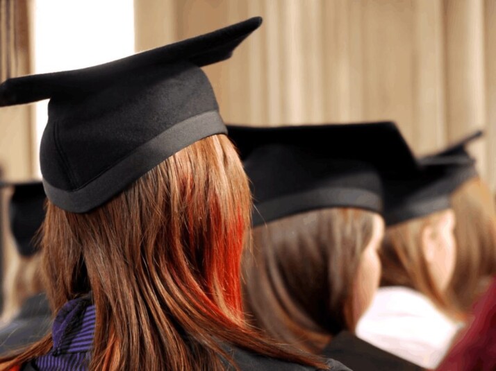 a woman with red dyed hair, wearing a graduation cap.