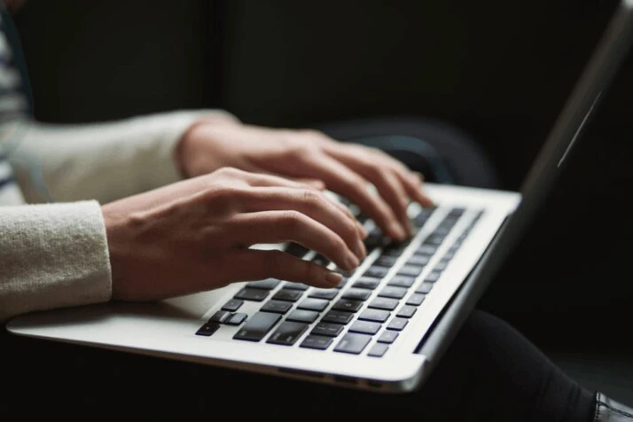 a woman writing something on her Macbook device by Apple.