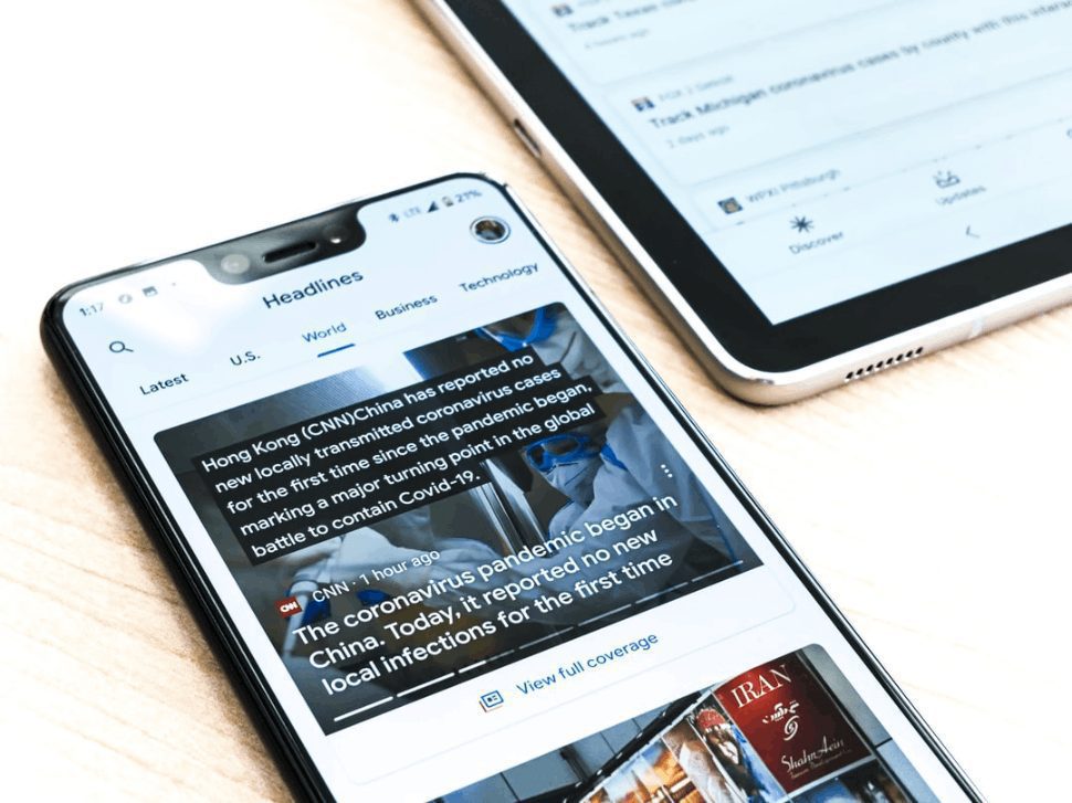 A silver iphone 6 on a light brown wooden table showing news headlines