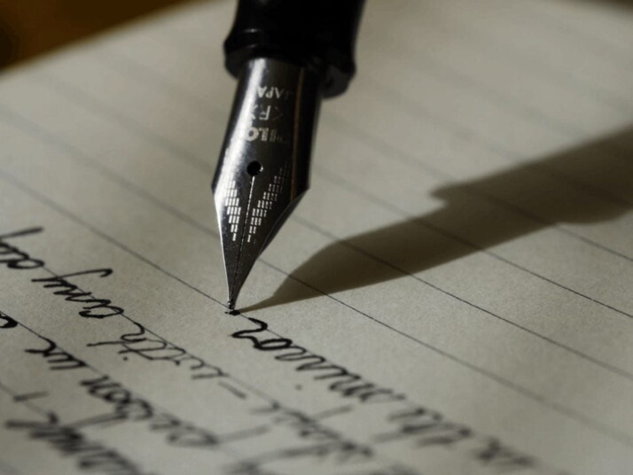 A fountain pen with its tip on a black lined paper