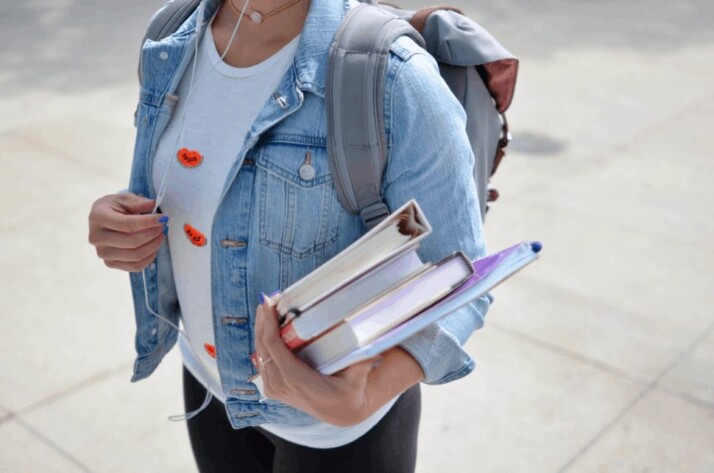 woman wearing blue denim jacket holding book with backpack behind