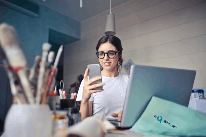 woman in white shirt using smartphone and a laptop on office table