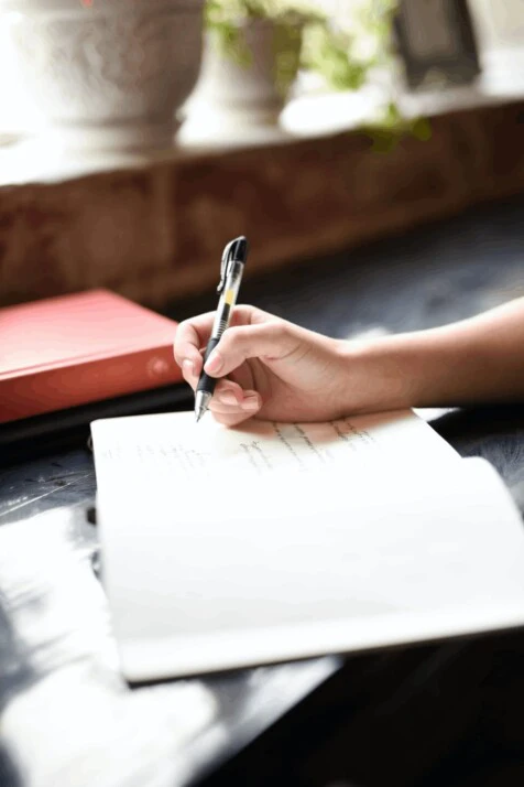 Feminine hand holding a black ink ballpen writing on a journal