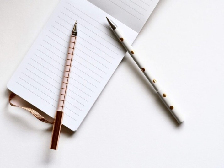 Two white and beige pens on a lined notebook.