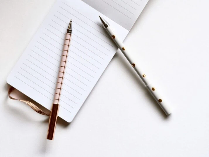 Two white and beige pens on a lined notebook.