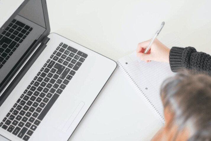 woman writing on notebook with a laptop in front of her