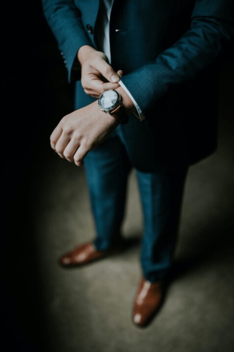man wearing a black suit, brown leather shoes and a watch.