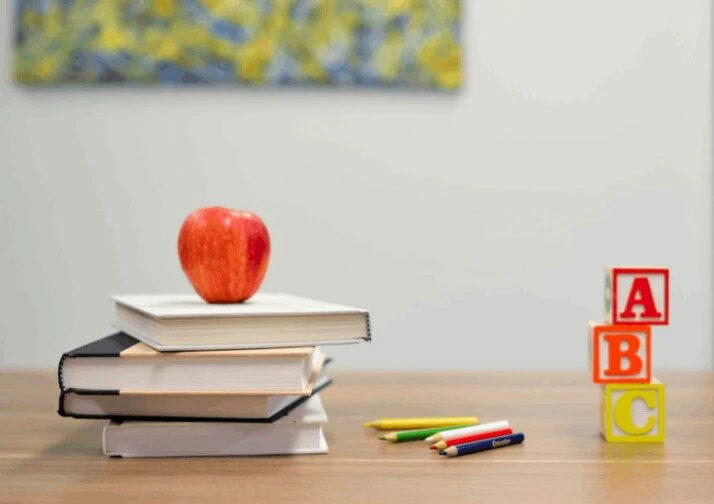 A red apple fruit with a pile of books on a wooden table
