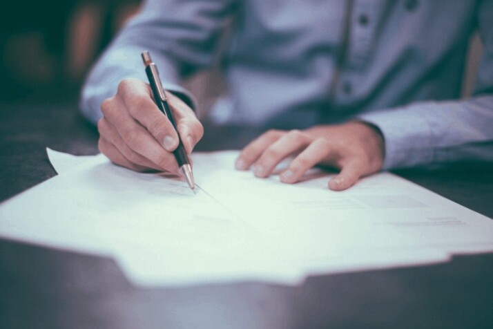 man wearing blue shirt, writing on paper with bold pen