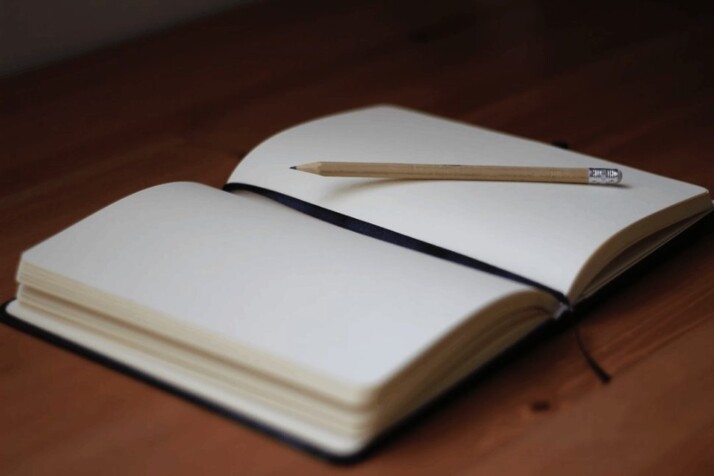 brown pencil and white opened book on brown table