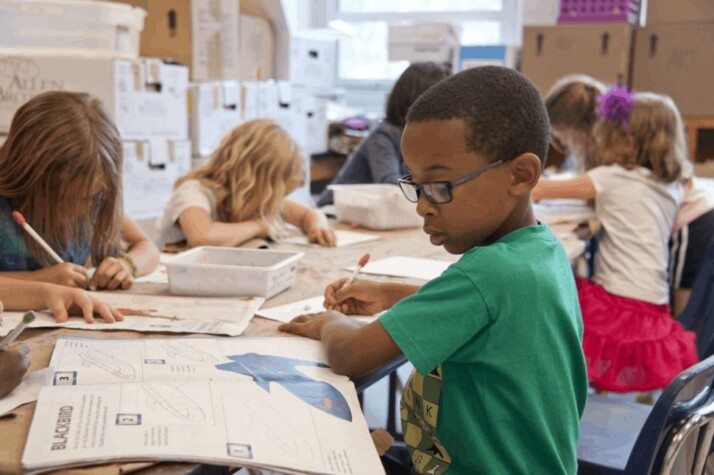 A boy in green sweater writing on white paper