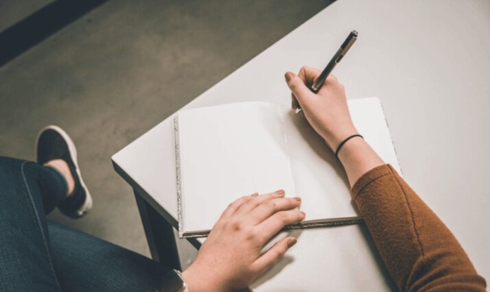 A person in brown garment is writing on a white paper