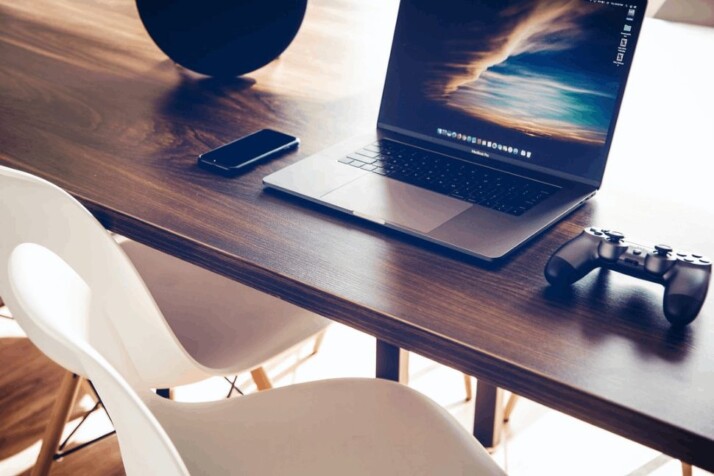 A turned on MacBook Pro with a controller on the right over a wooden table. 