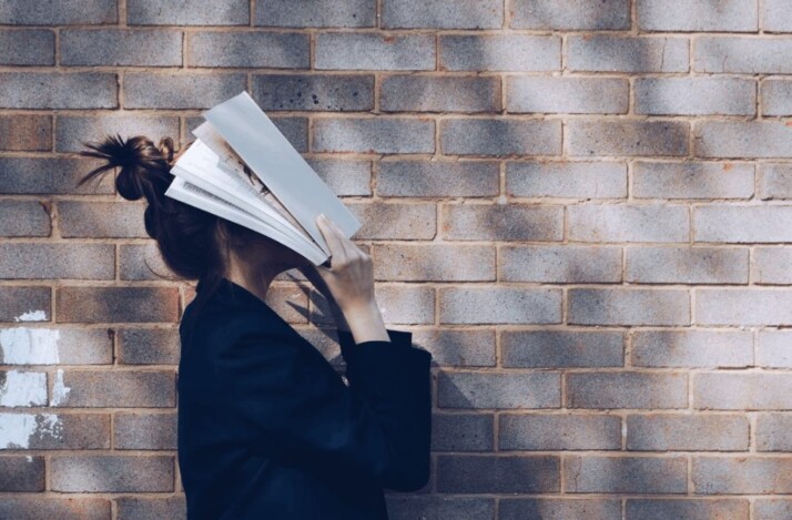 A woman covering her face with a white book.