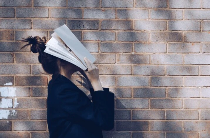 A woman covering her face with a white book.