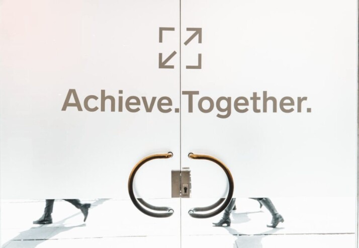 a frosted glass door with two handles that says Achieve. Together.