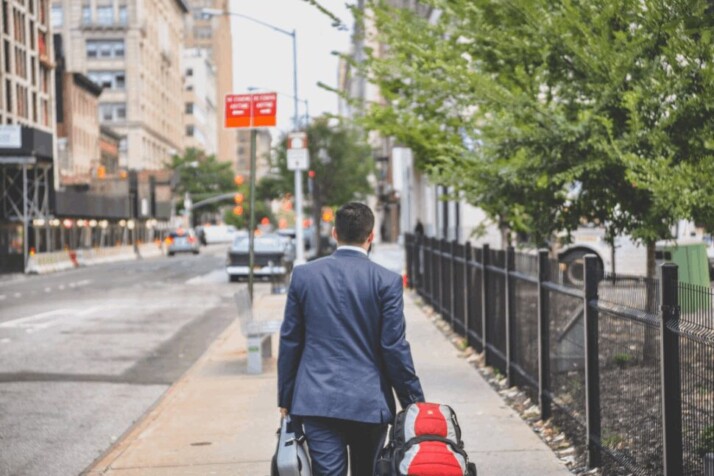 person in a black suit jacket with a red bag walking away.