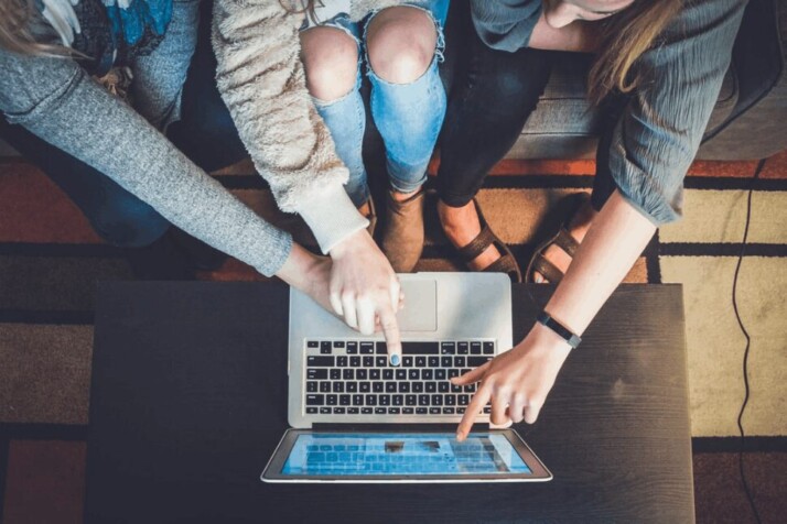 Three people working together on a laptop while pointing at something on the screen.