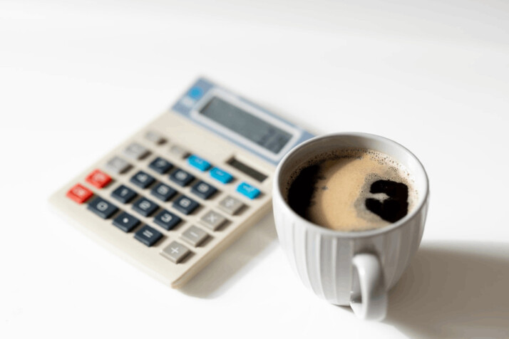 a typical calculator next to a white cup filled with coffee, possibly Americano.