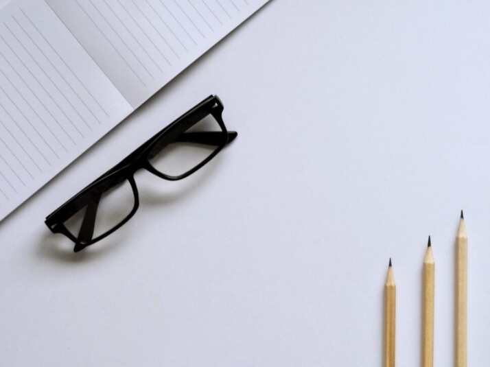 Black eyeglasses next to three pencils and a notebook.