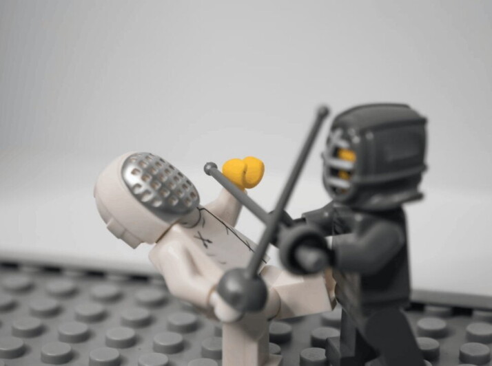 Two Lego figurines fighting or attacking each other in a game of fencing.