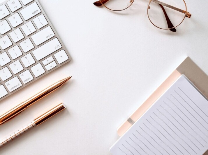 A pen near a notebook, a pair of glasses, and a keyboard.