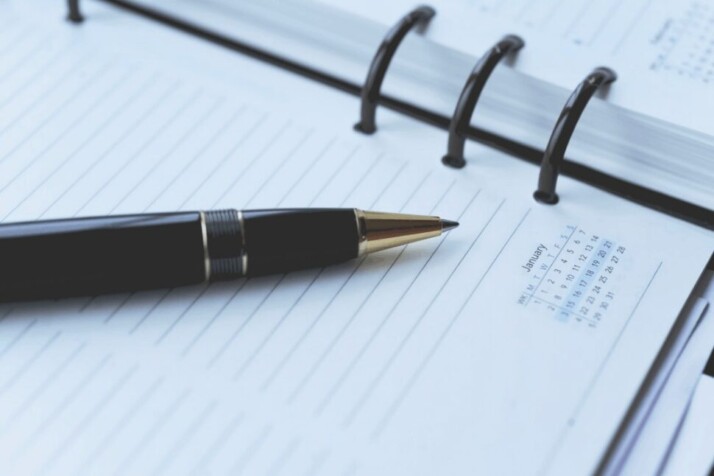 A black ballpoint pen on top of a white spiral notebook