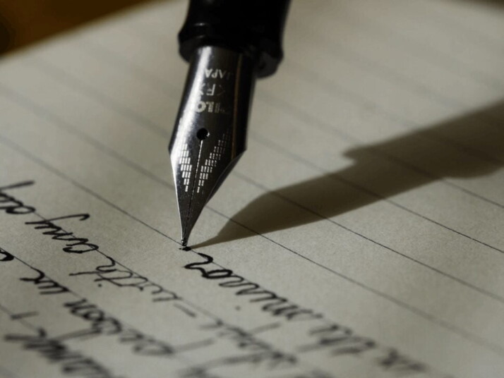 Fountain pen being used to write on a sheet of paper.