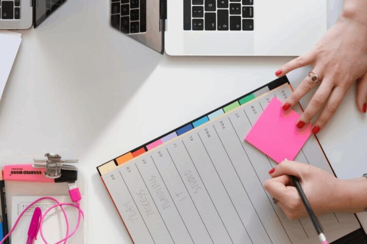 A person writing something on a pink sticky note.